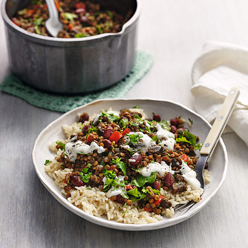 Slimming World lentil chilli with rice, served in a while bowl. The background is a white tabletop.